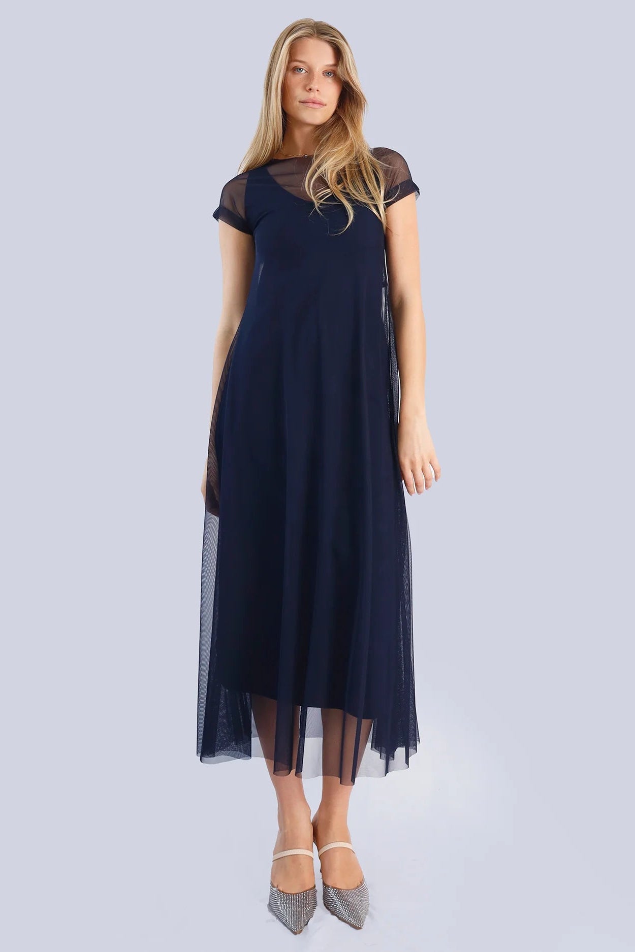 Woman wearing a navy blue dress with sheer sleeves and hem on a light gray background.