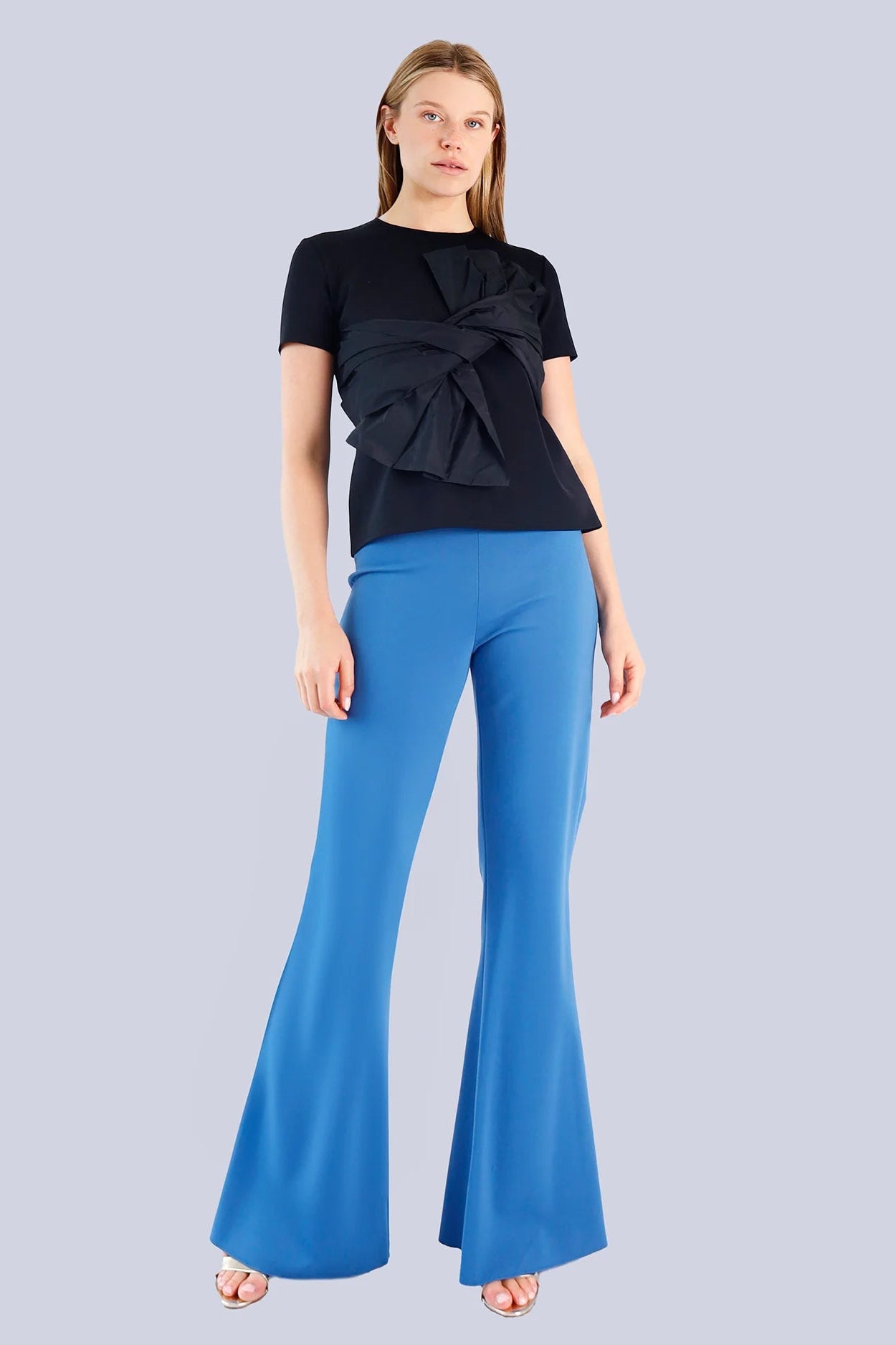 Woman wearing a black top and blue flared pants on a light gray background