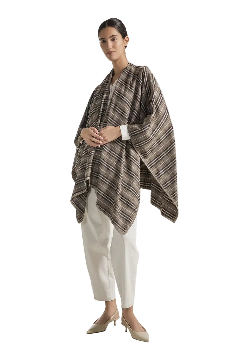 Woman wearing a patterned poncho over a white outfit on a light gray background.