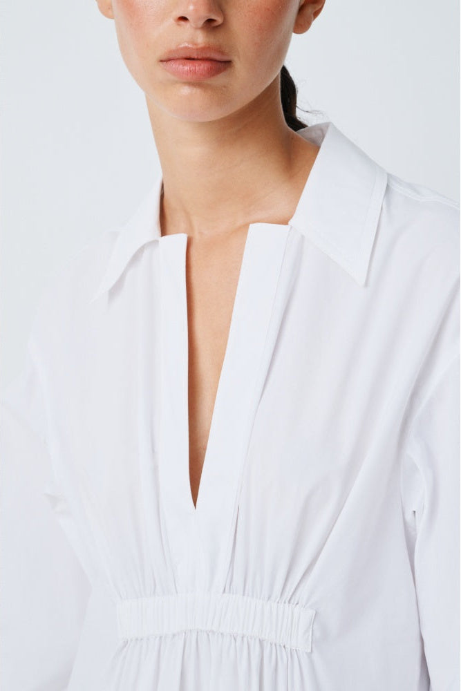 Close-up of a woman wearing a white v neck dress on a plain background.