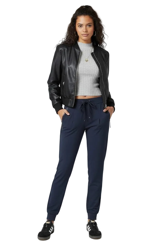 Woman wearing a black leather jacket, gray sweater, and navy jogger pants on a white background.