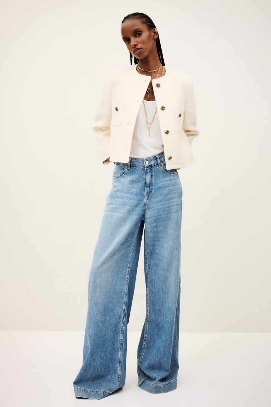 Woman wearing a white jacket and blue jeans on a white background.