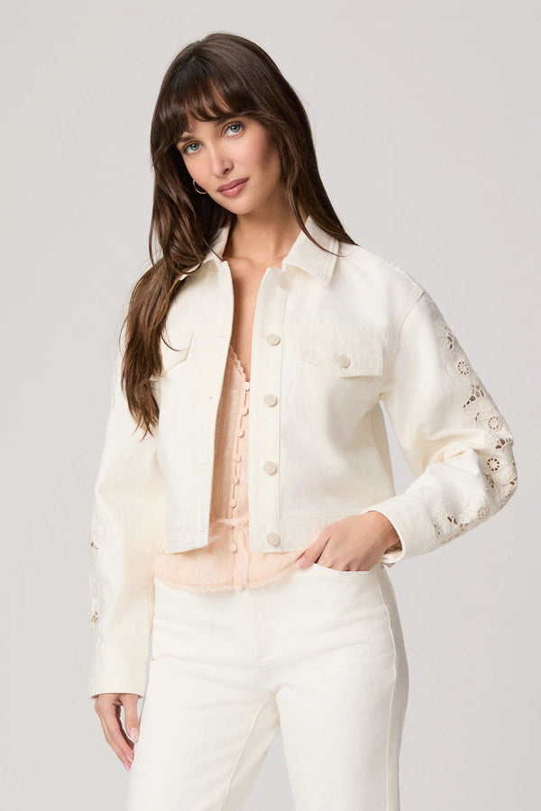 Woman wearing a white jacket with lace details on a plain background.