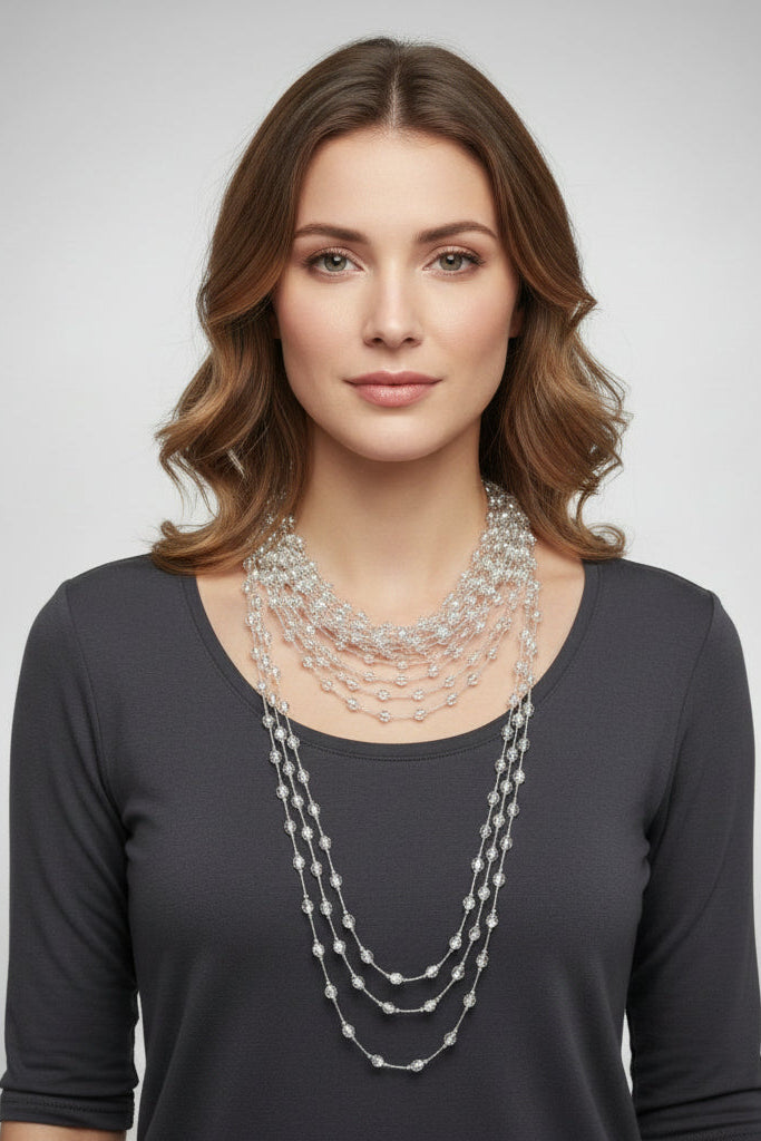 Woman wearing a layered silver necklace against a plain background.