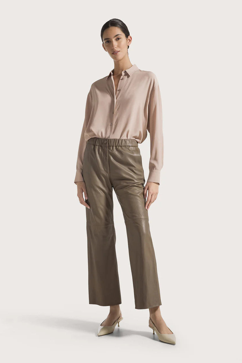 Woman wearing a beige blouse and taupe colored leather pants on a light background.