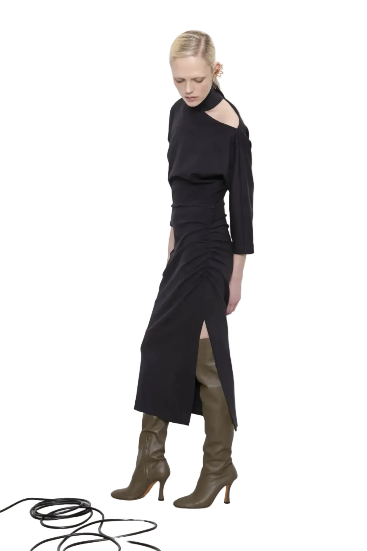 Woman wearing a black dress with a high slit and green boots on a white background.