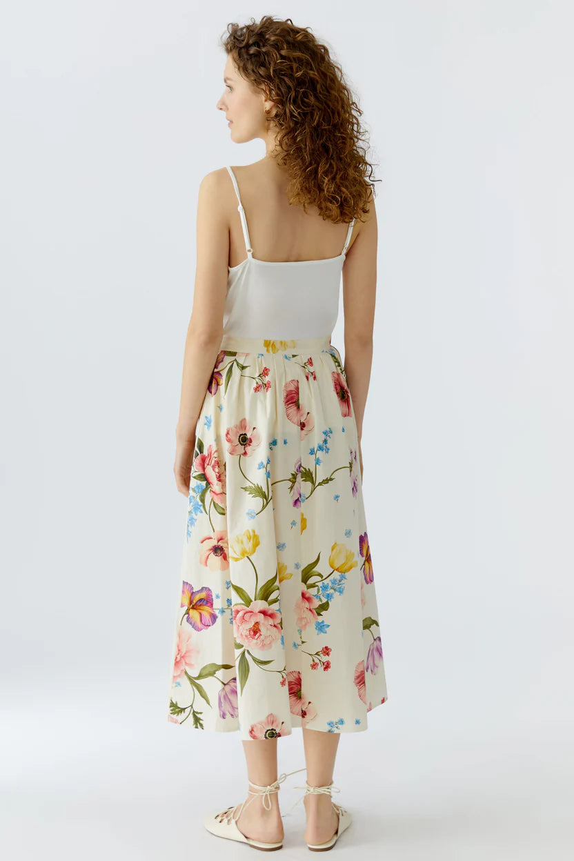 The back of a woman wearing a white top and floral skirt on a white background.