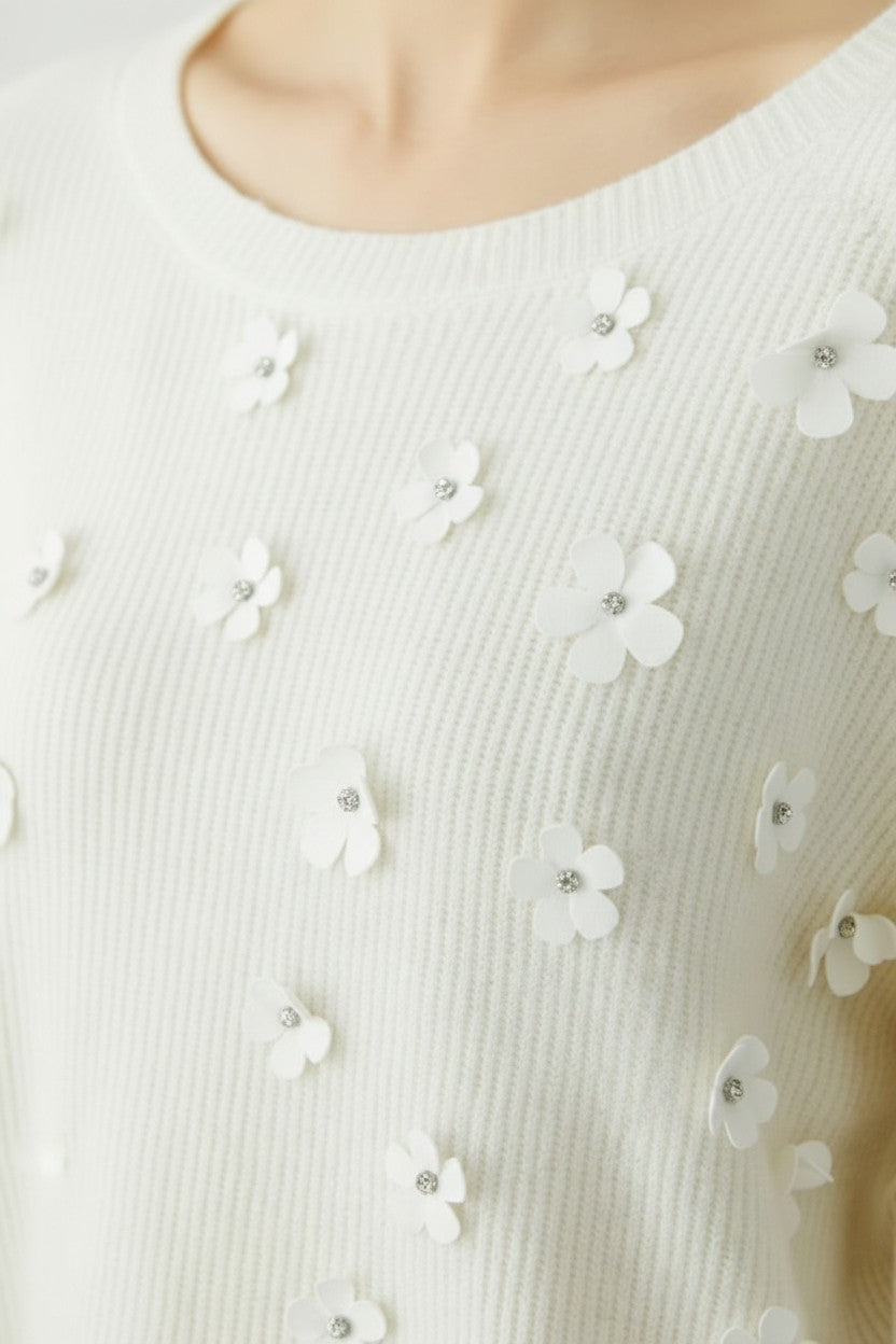 Close-up of a sweater with floral embellishments on a neutral background.