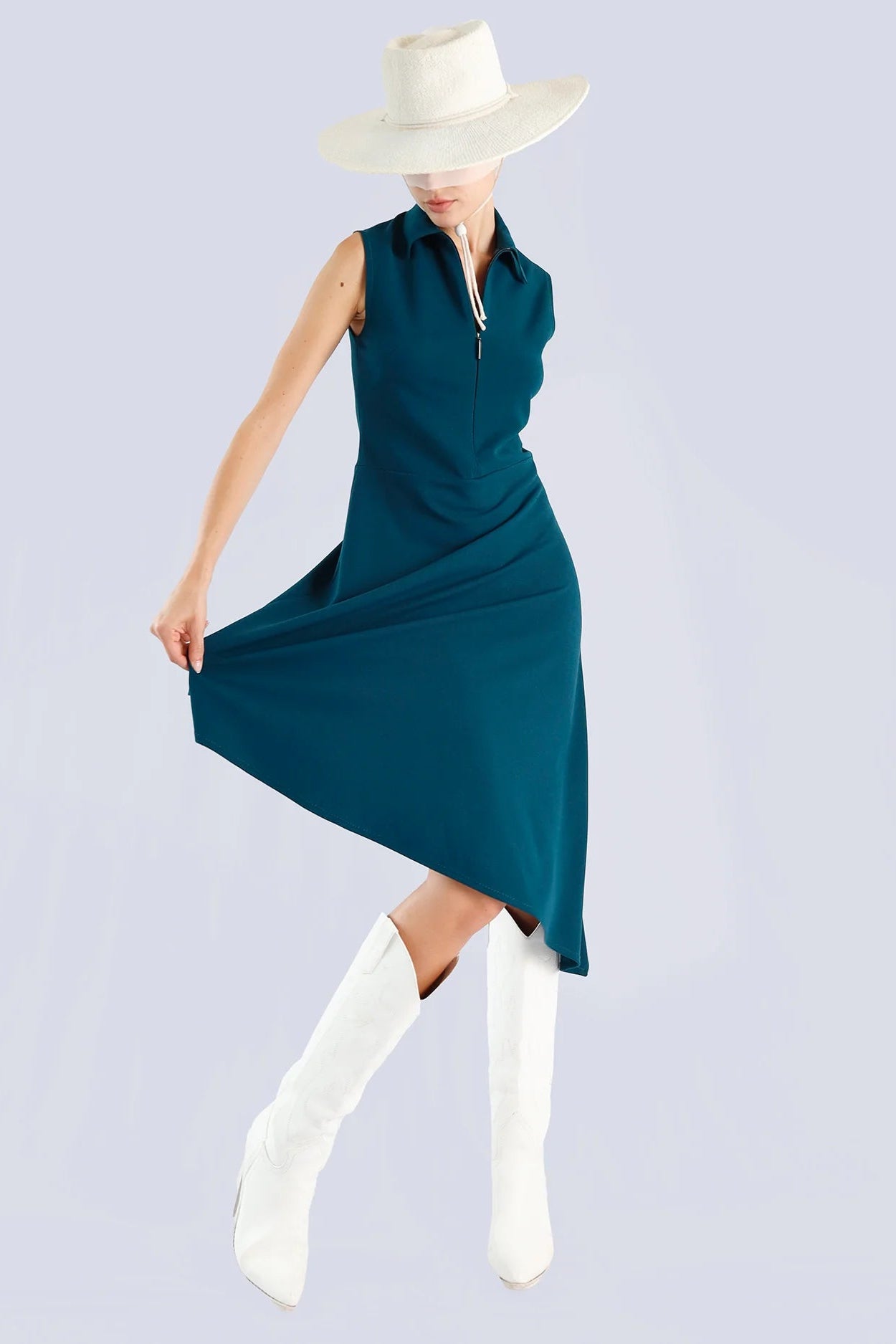 Woman wearing a teal sleeveless dress, white boots, and a white hat on a light gray background.