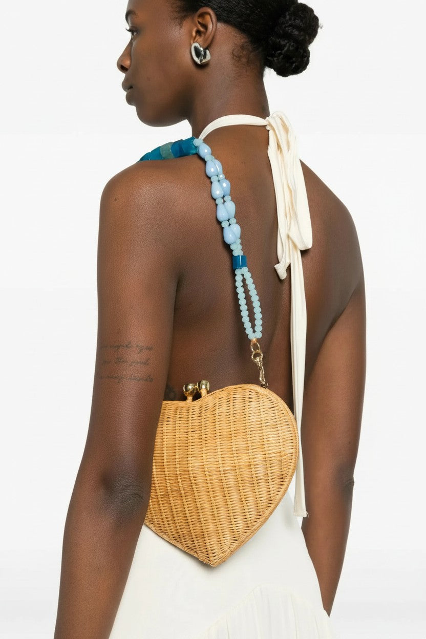 Woman wearing a heart-shaped wicker handbag with a white strap and blue beads.