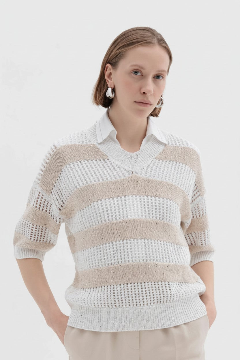 Woman wearing a white and beige striped sweater on a plain background.