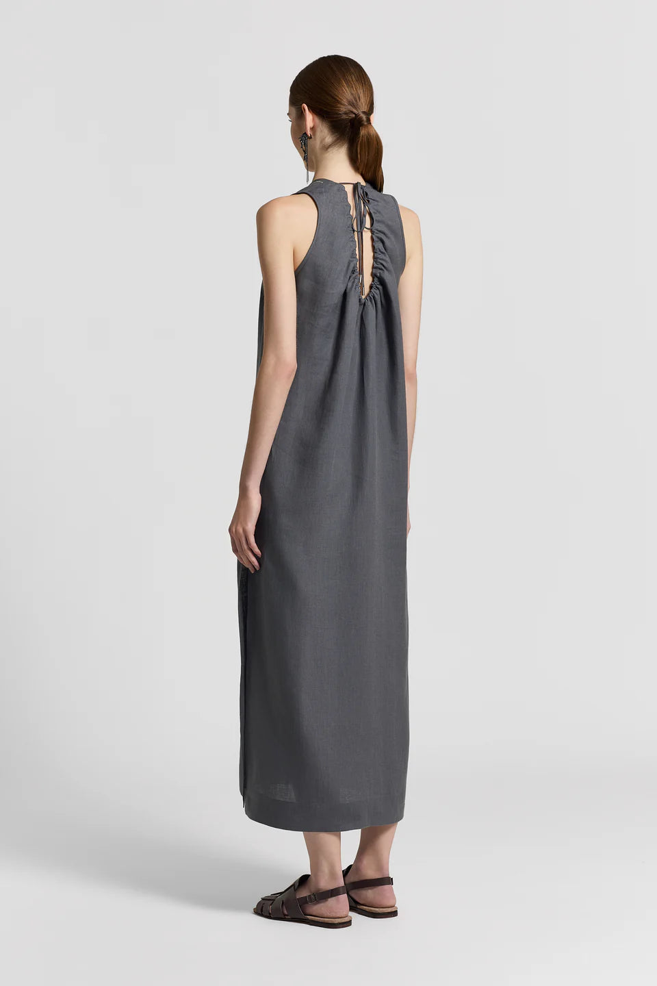 The back of a woman wearing a blue gray sleeveless dress with a cut-out back on a white background.