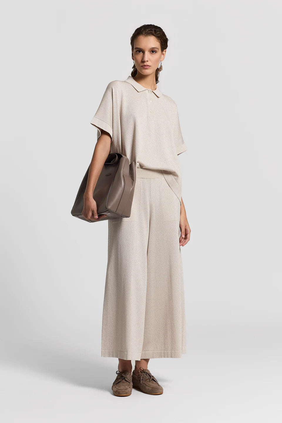 Woman wearing a beige outfit with a brown bag on a white background.