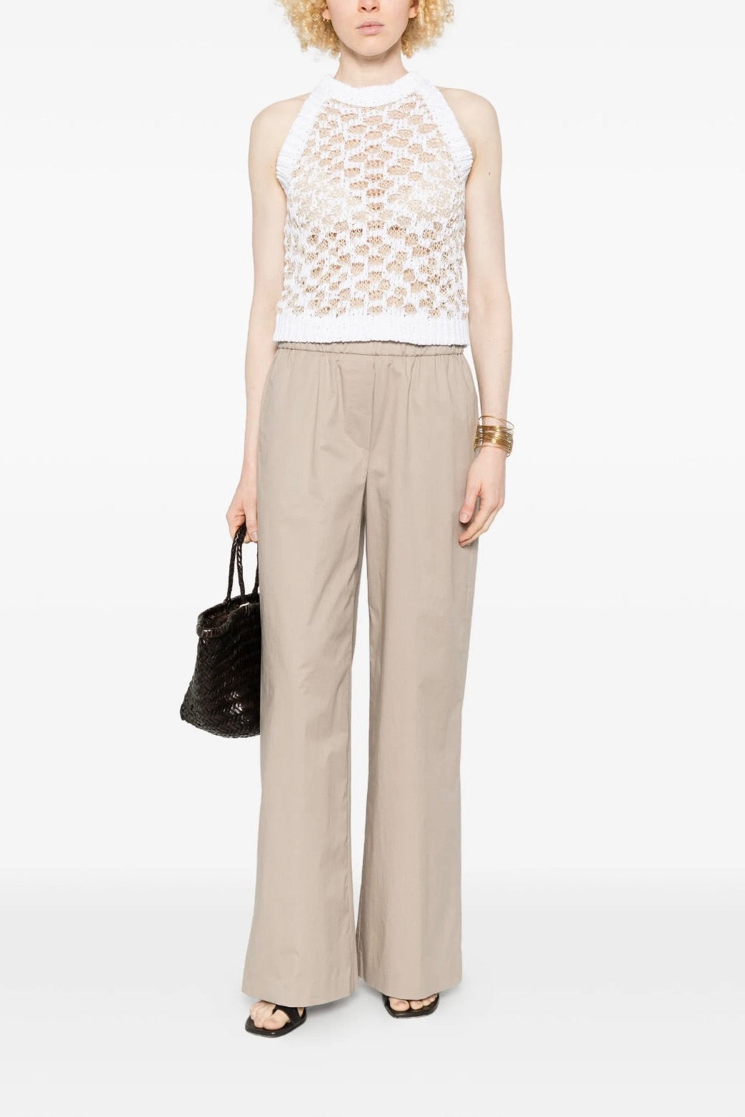 Woman wearing a white crochet top and beige wide-leg pants on a white background.