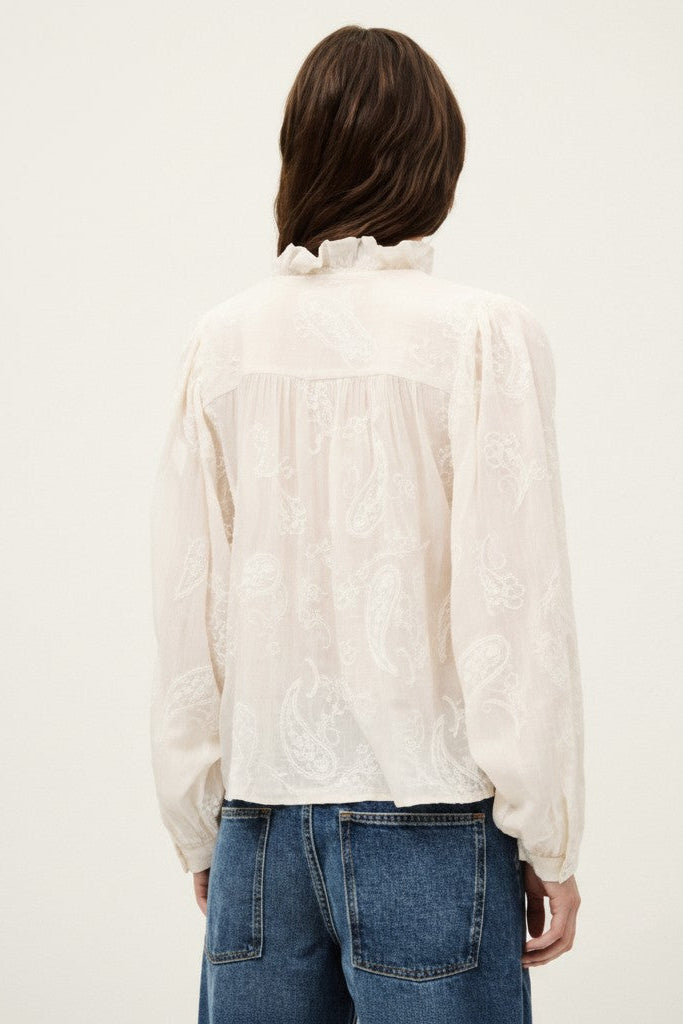 Back of a woman wearing a white blouse and blue jeans on a plain background.