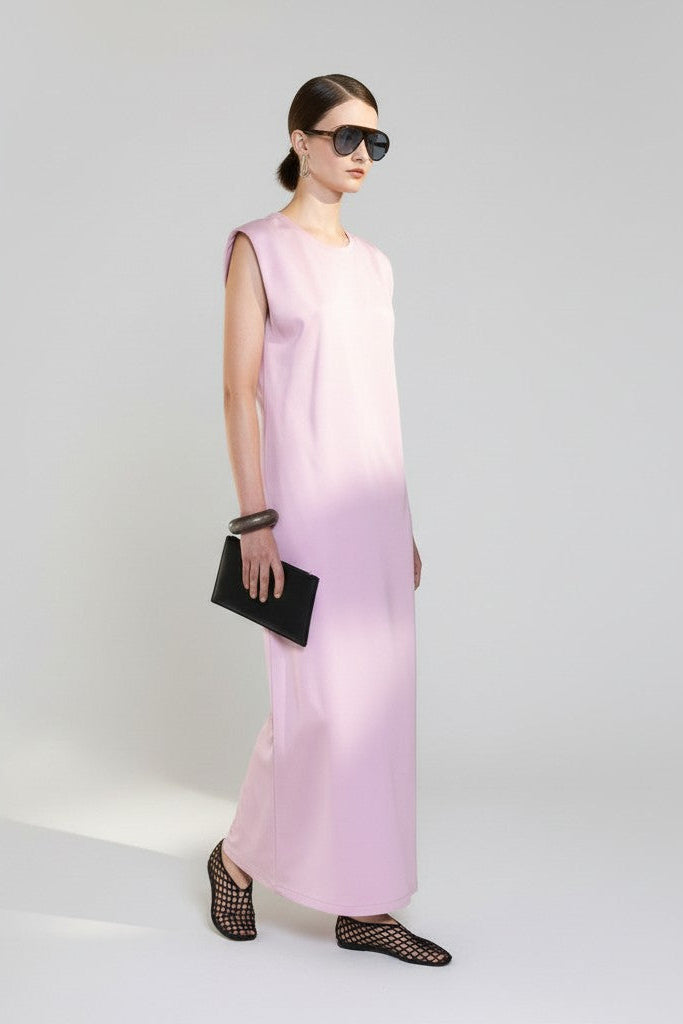 Woman wearing a pink gradient dress with black shoes and sunglasses on a white background