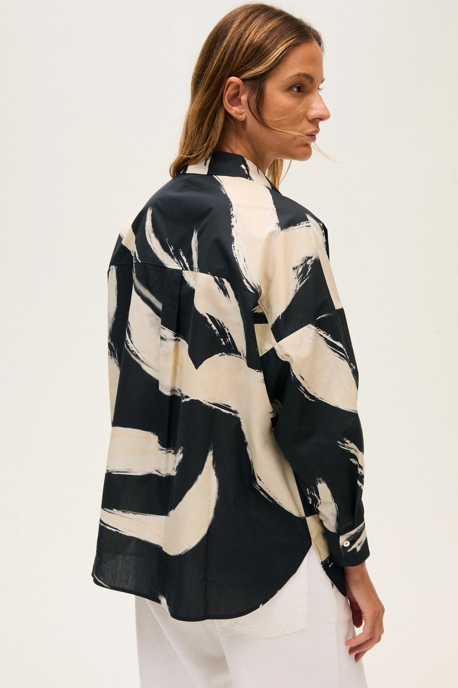Back of a woman wearing a black and off-white abstract patterned blouse on a white background.