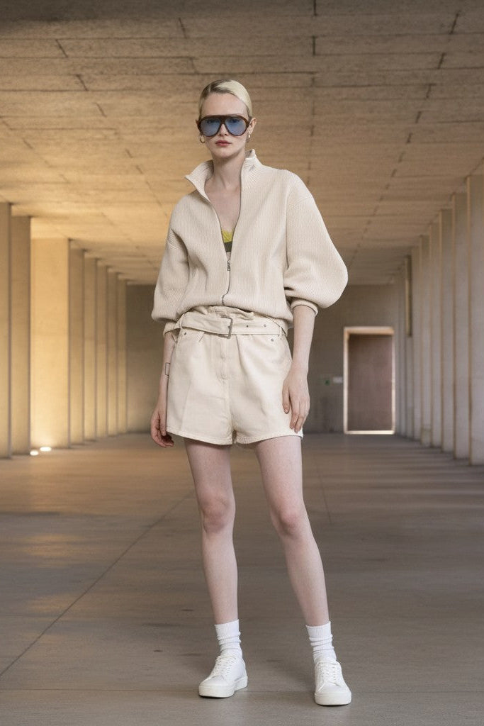 Woman in a beige outfit standing in a long, narrow hallway with concrete walls and ceiling.