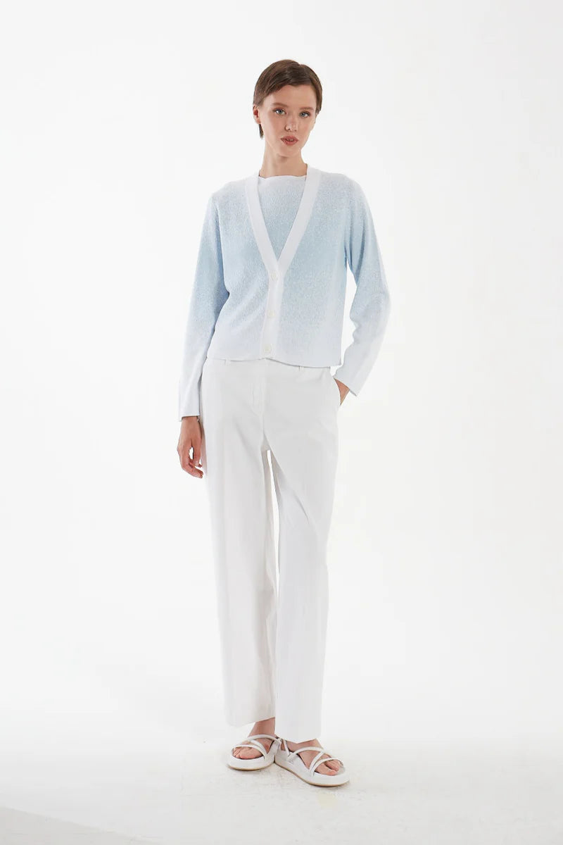 Woman wearing a light blue cardigan and white pants on a white background.