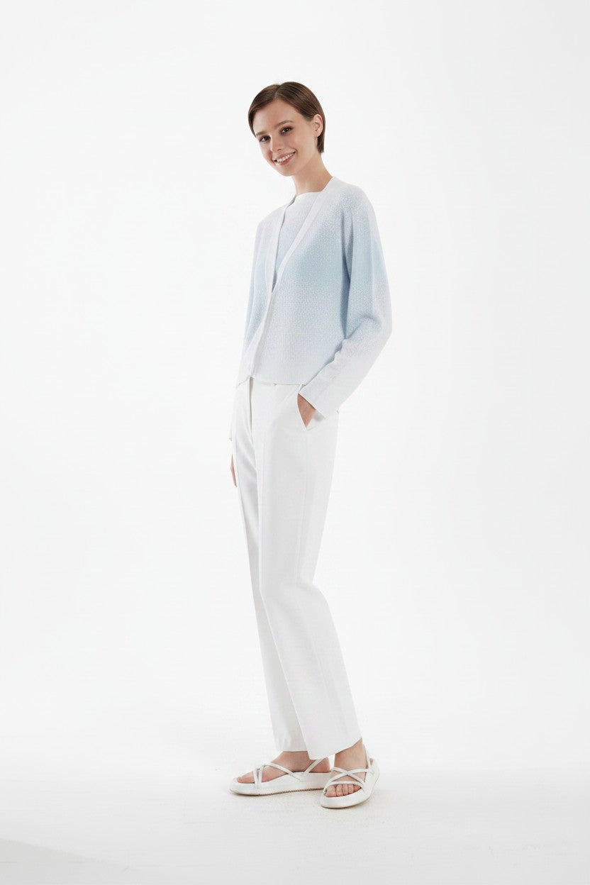 Woman wearing a light blue cardigan and white pants on a white background.