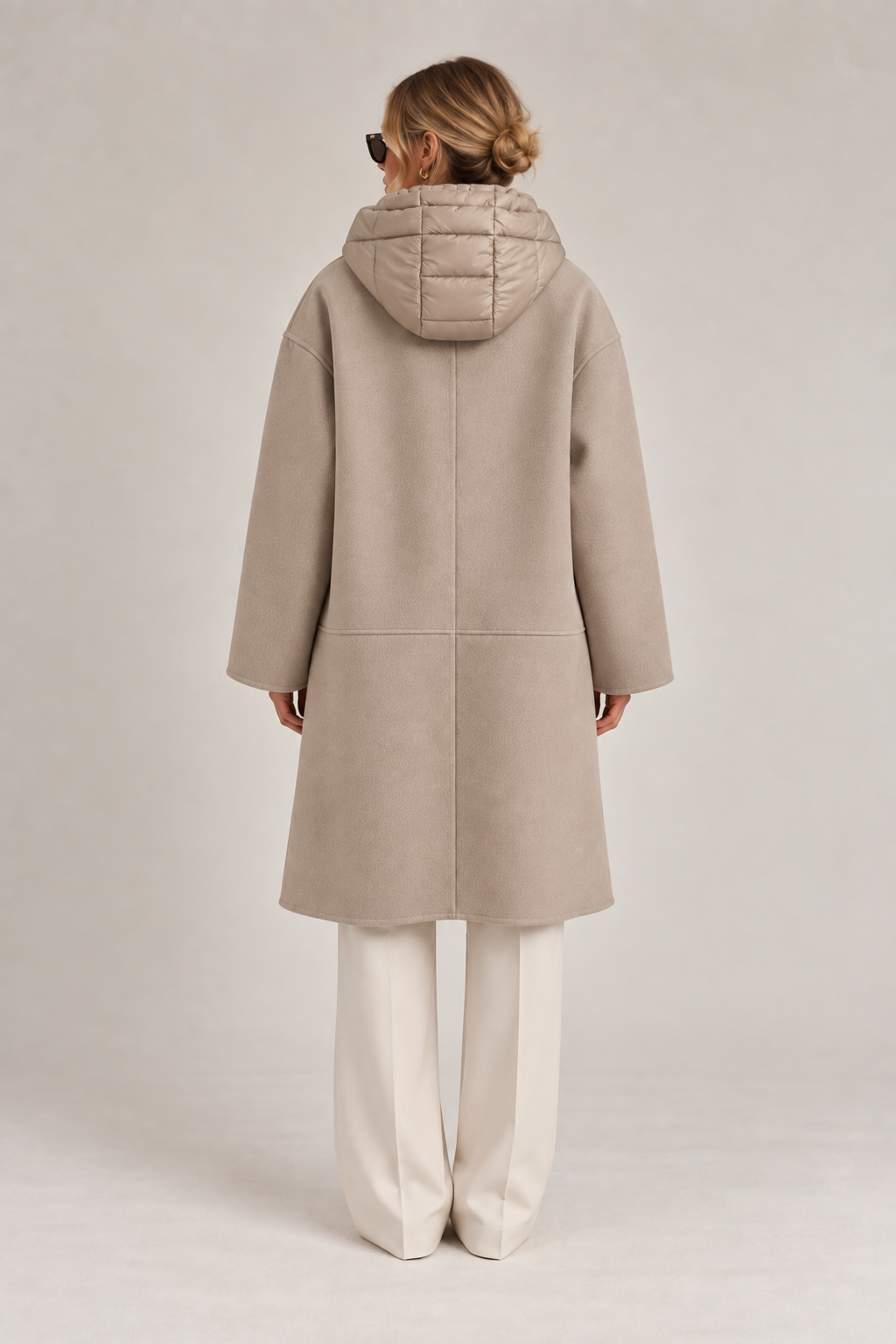 Back view of model wearing a taupe long coat with quilted hood, center back seam, and relaxed oversized silhouette.