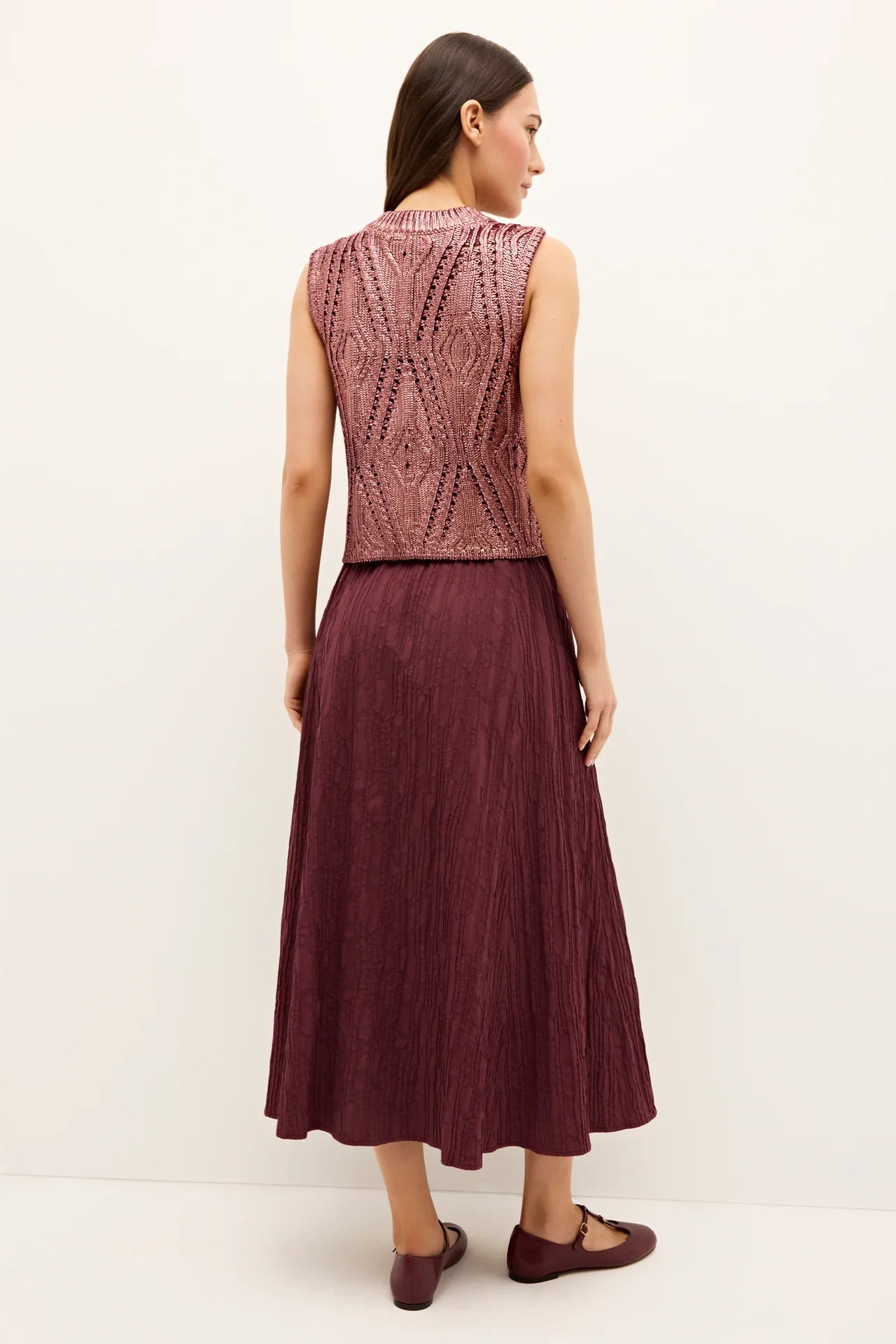 Woman wearing a patterned sleeveless top and burgundy skirt on a white background.