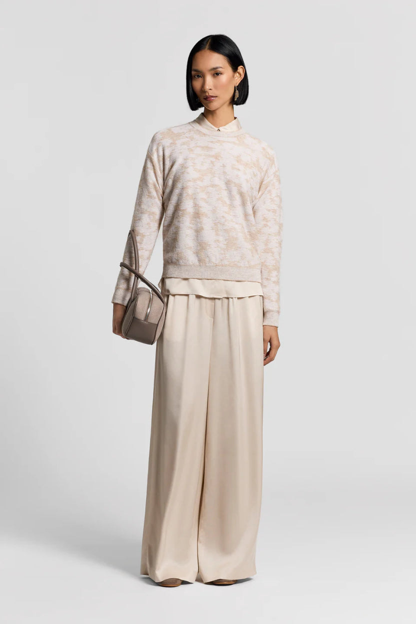 Woman wearing a beige patterned top and beige wide-leg satin pants with a handbag on a white background.