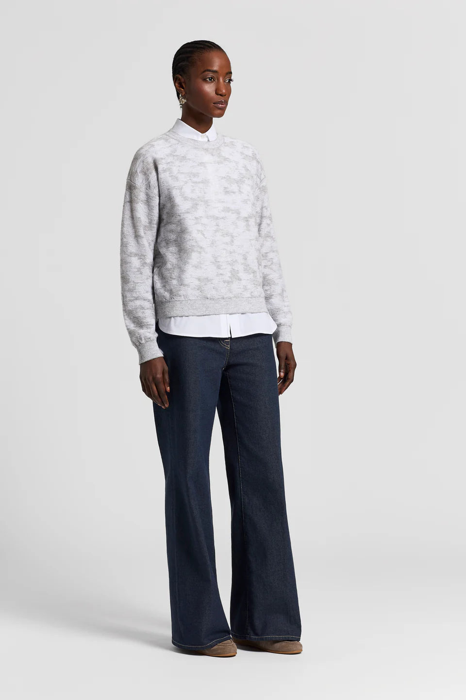 Woman wearing a white sequinned sweater and dark blue pants on a light gray background.