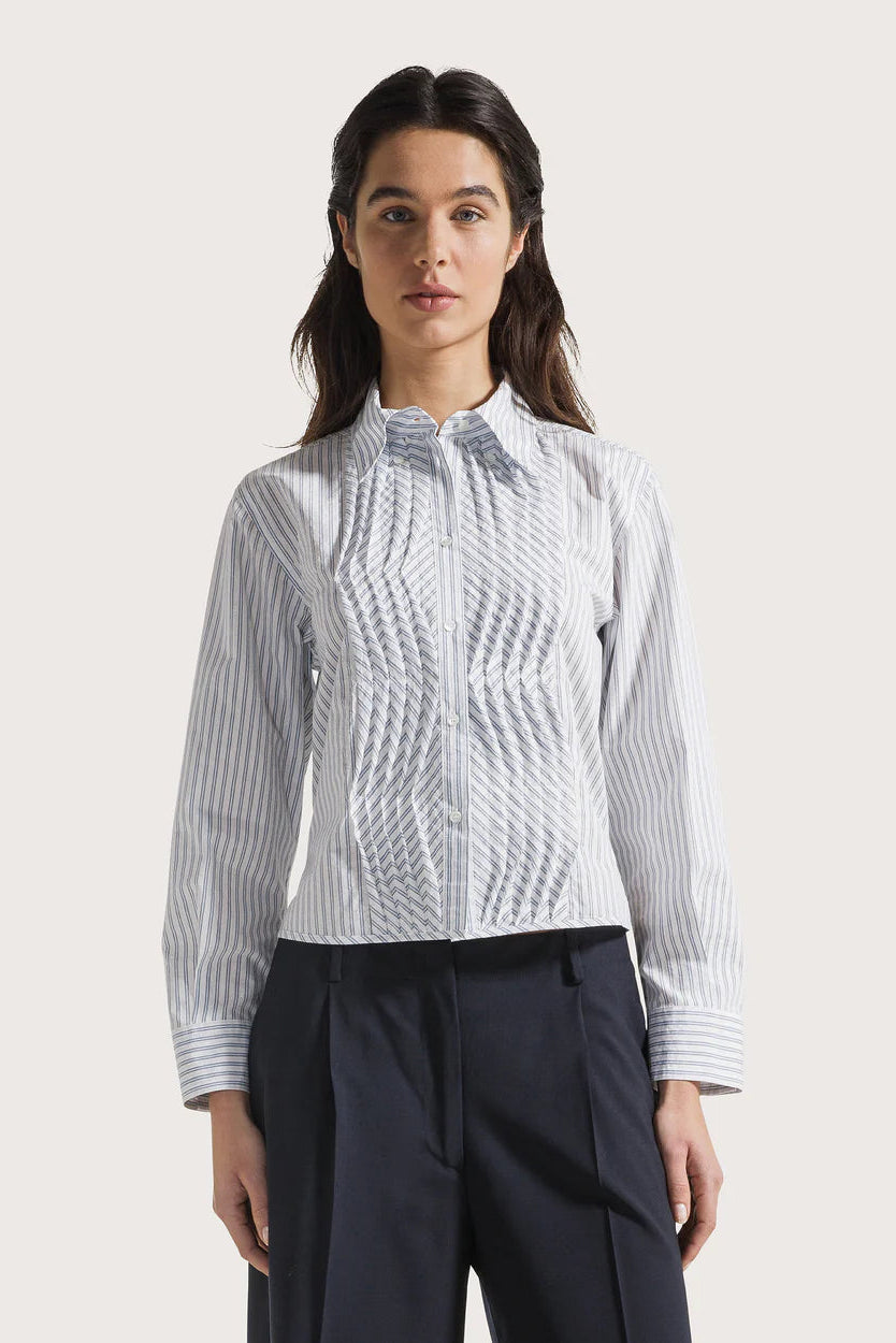 Woman wearing a white blouse with a textured pattern and dark pants on a light background