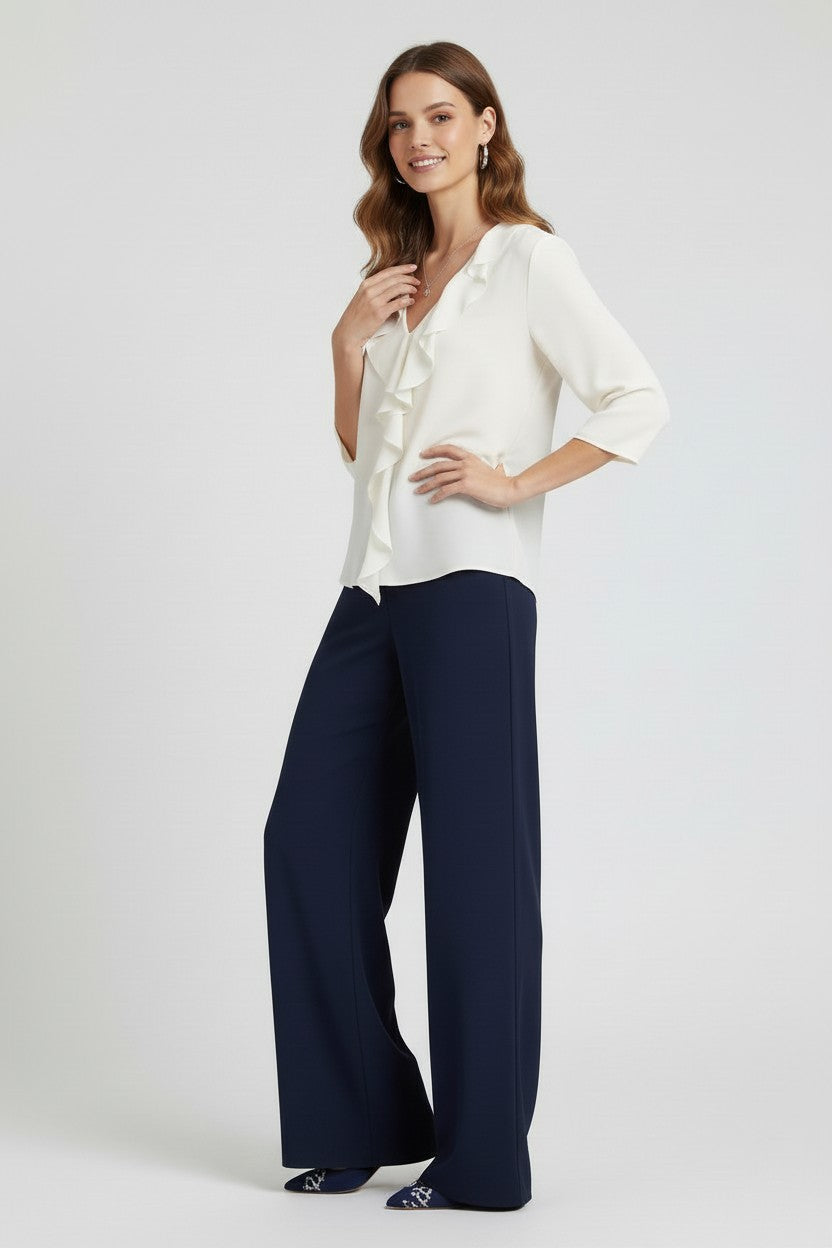 Woman wearing a white blouse and navy pants on a plain background.