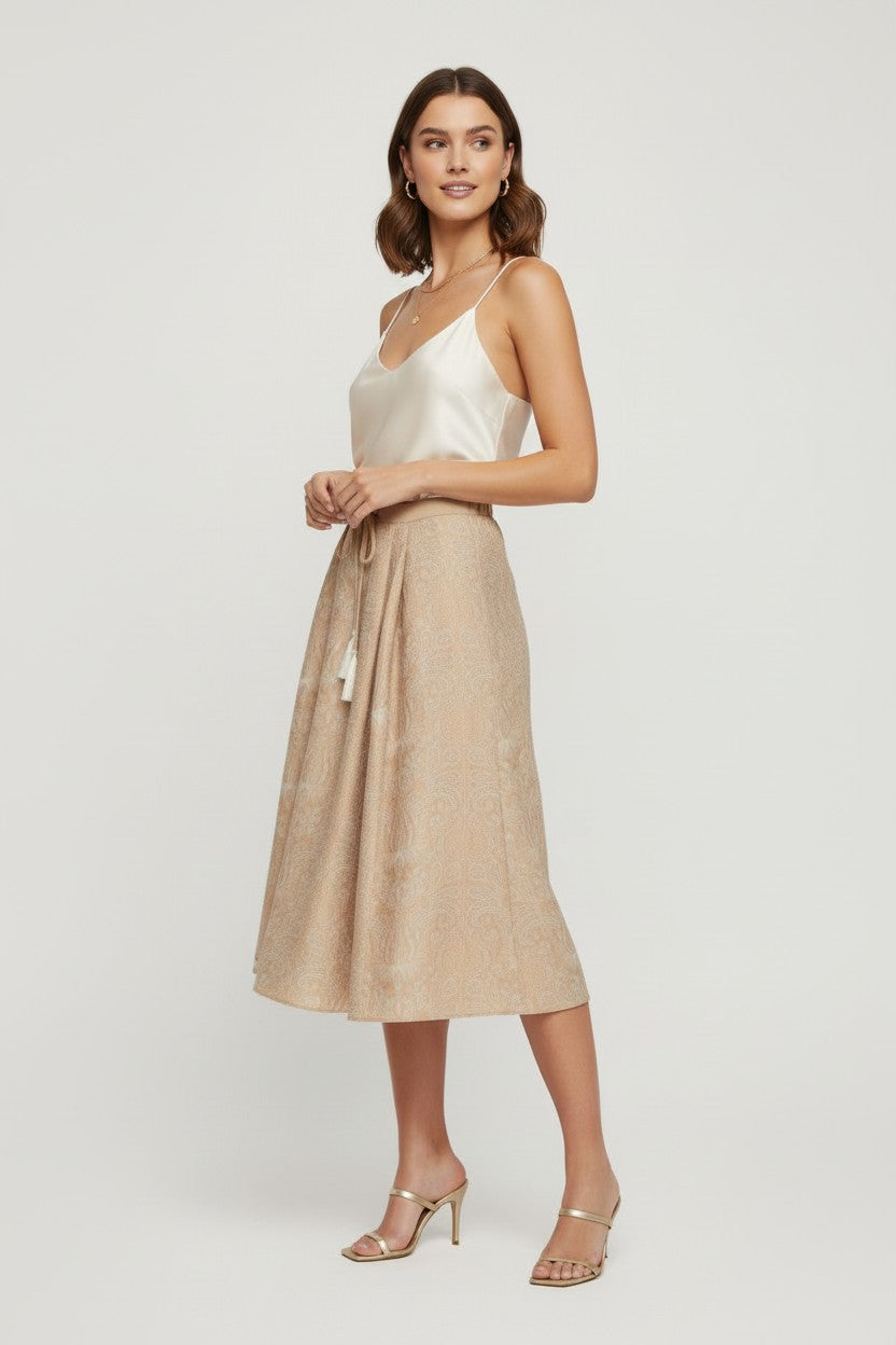 Woman wearing a cream sleeveless top and beige skirt on a plain background.