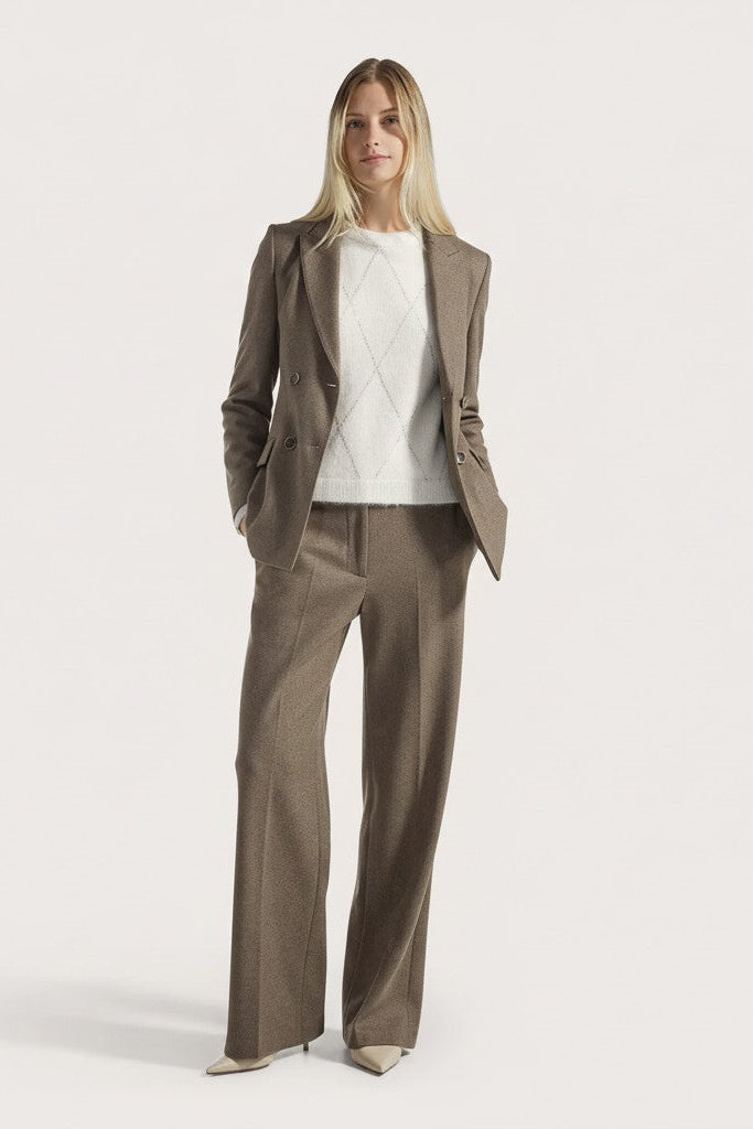 Woman wearing a brown suit with a white sweater on a light gray background.