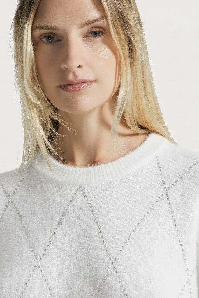 Woman wearing a white sweater with a sparkle pattern against a light background.