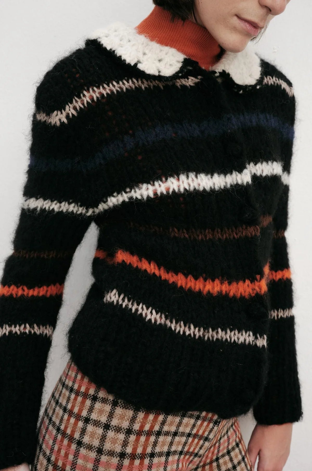 Woman wearing a black, white, and red striped sweater with plaid pants on a white background.