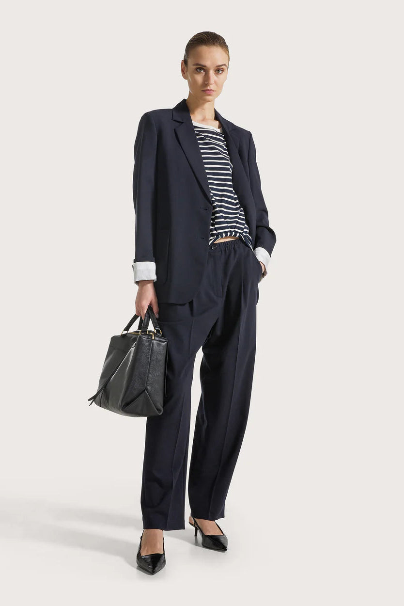Woman in a navy suit with a navy and white top holding a gray handbag on a light background.