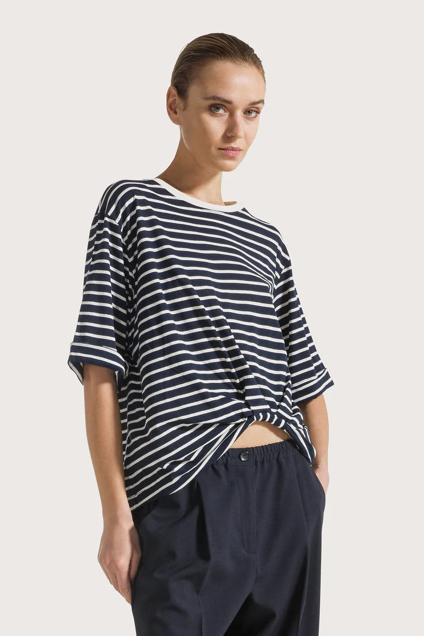 Woman wearing a navy and white striped shirt with a plain background.