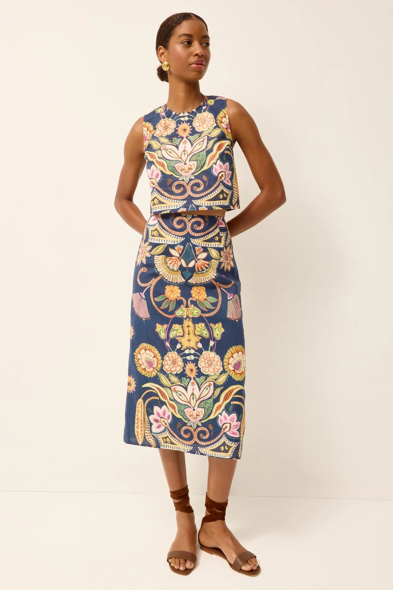 Woman wearing a colorful sleeveless top and skirt with floral patterns on a white background.