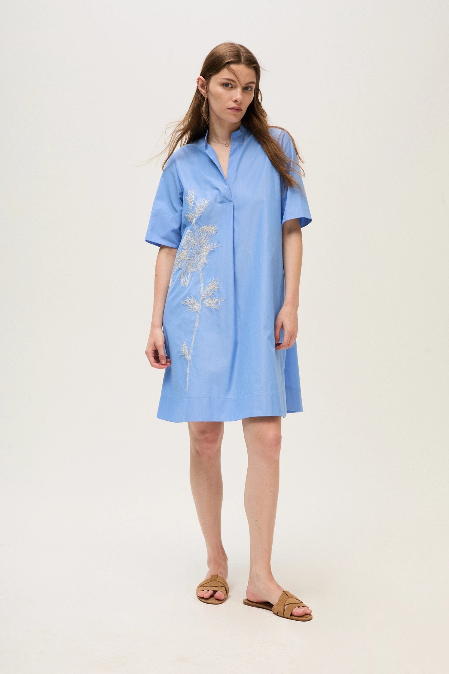 Woman wearing a light blue dress with floral embroidery on a white background.