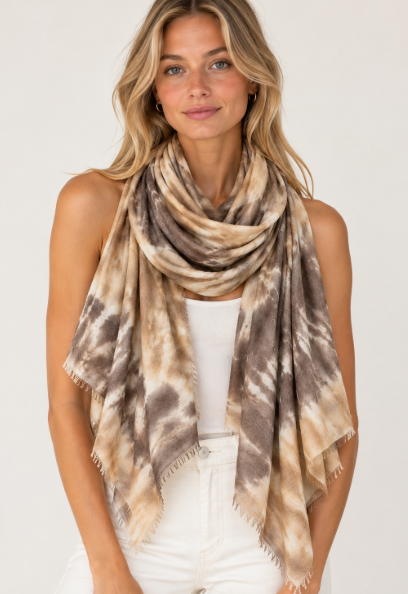 Front-facing blonde model wearing an earth-toned marbled scarf in shades of beige, taupe, cream, and brown, featuring a soft draped silhouette and delicate fringed edges, styled over a white outfit against a neutral studio background.