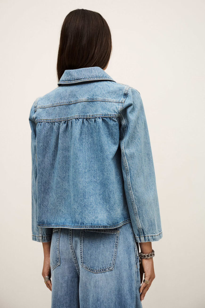 Womanwearing a blue denim jacket and jeans on a plain background.