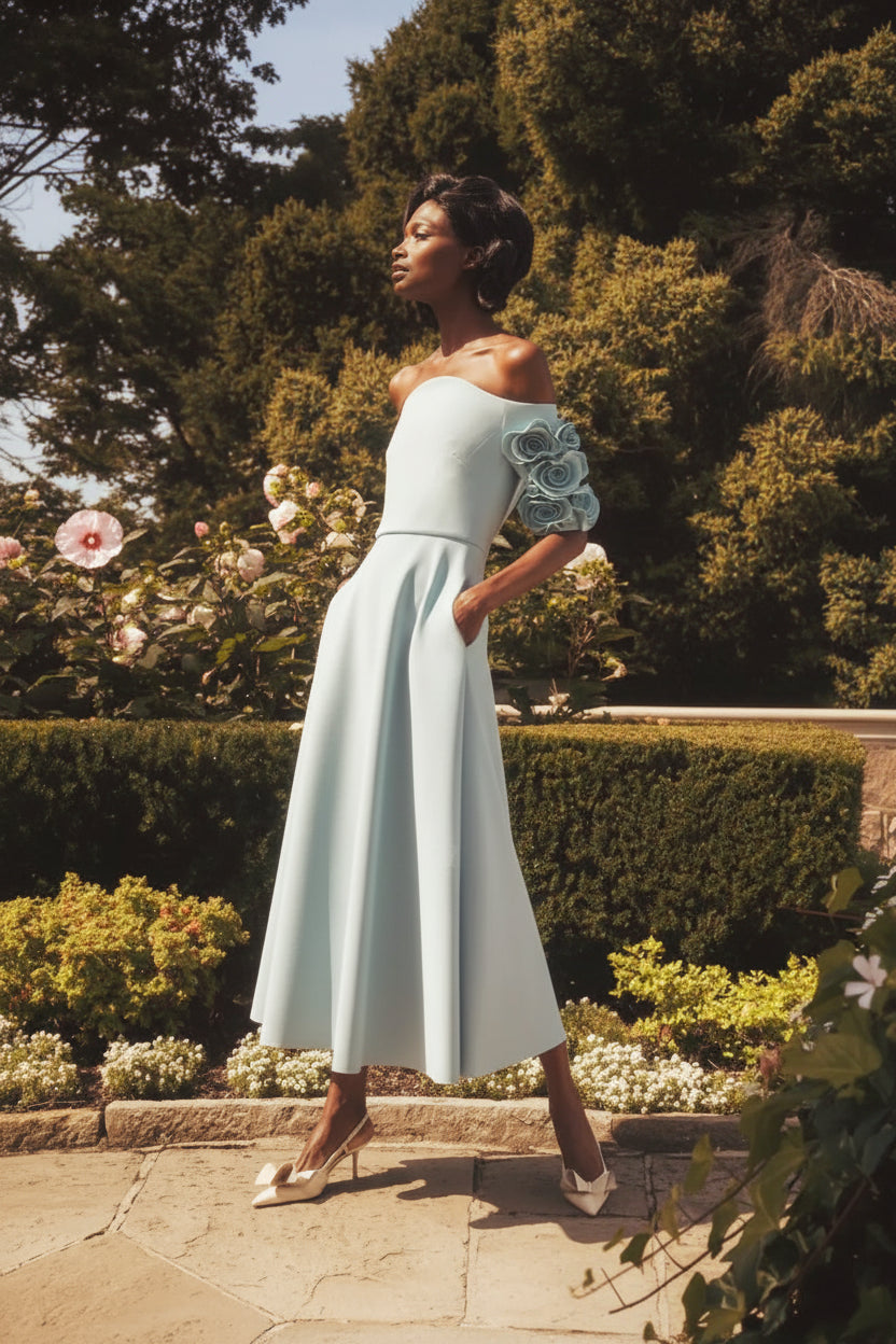 Woman in a light blue dress standing in a garden with greenery and flowers.