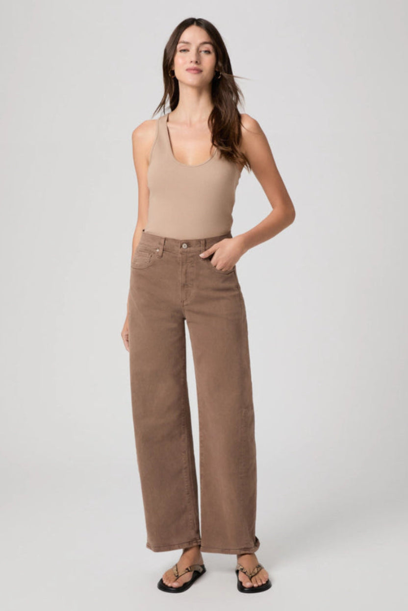 Woman wearing a beige tank top and brown jeans on a white background.