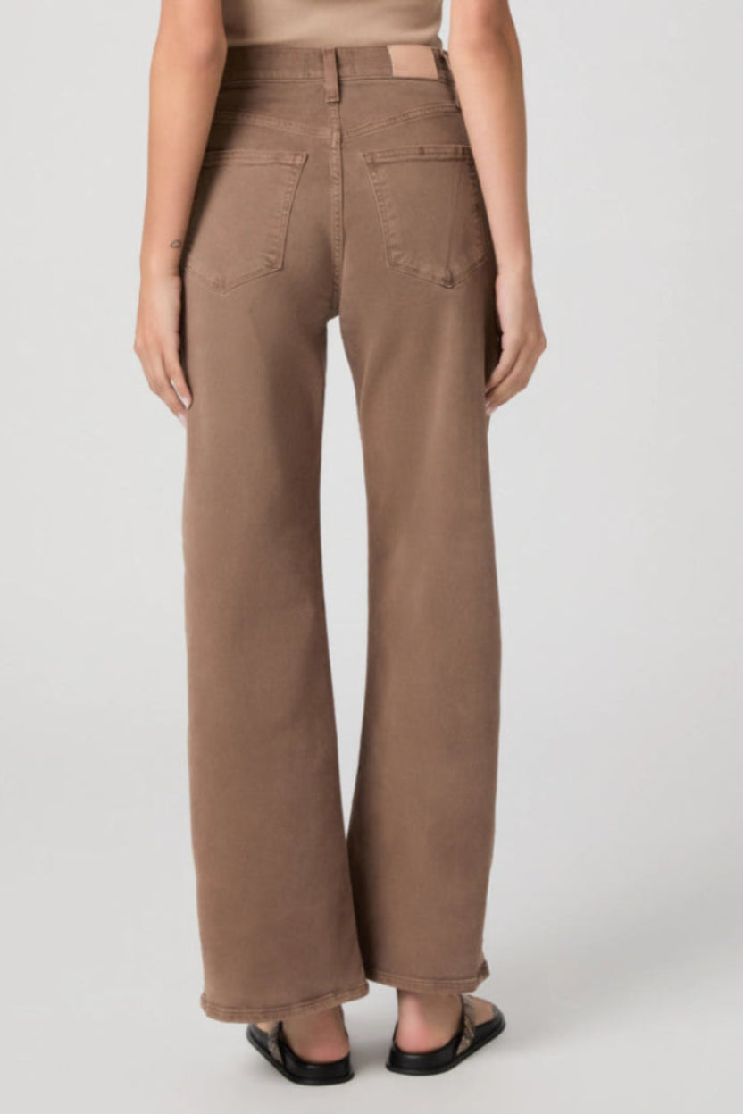 The back of a woman wearing brown wide-leg pants on a white background.