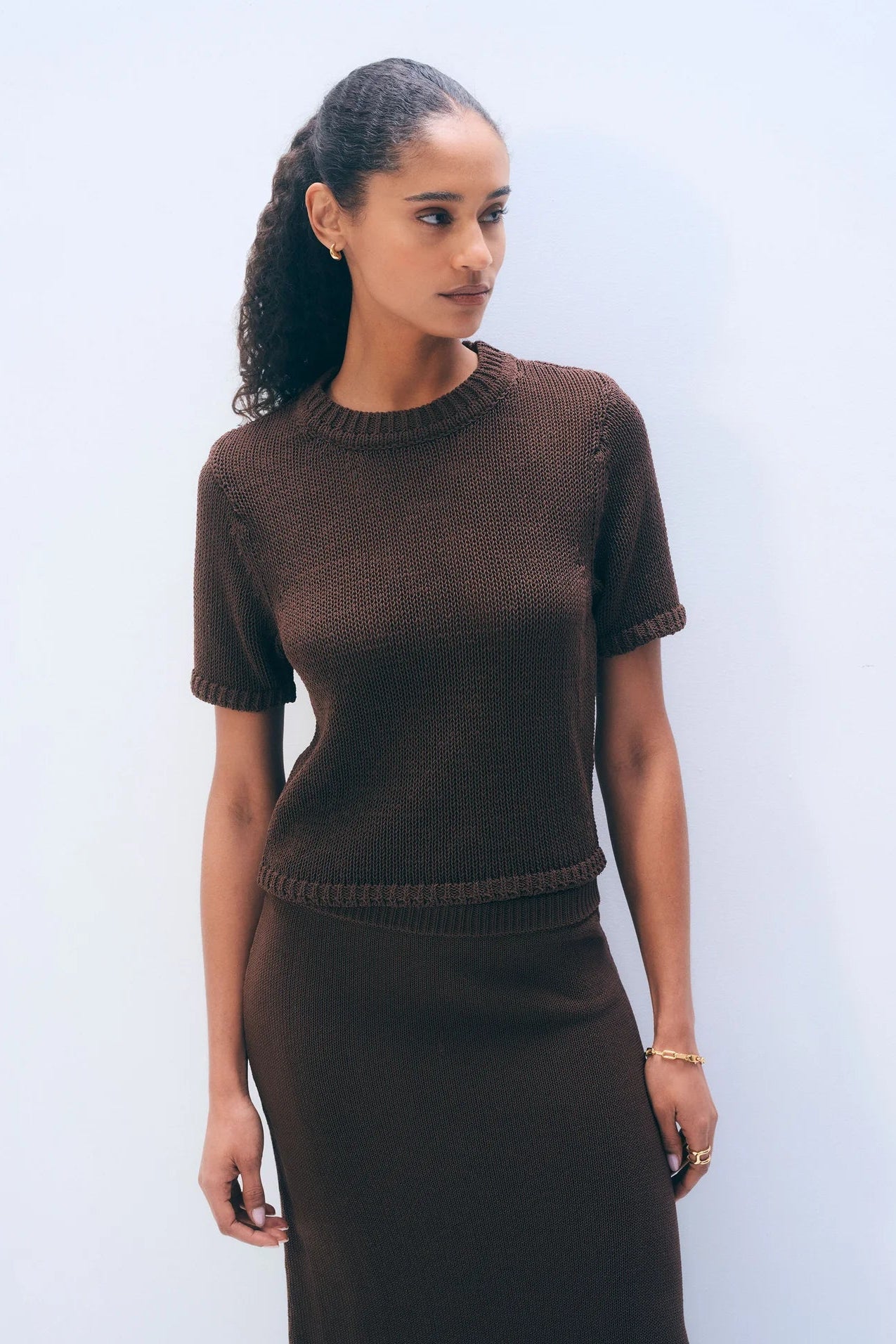 Woman wearing a brown short-sleeve top and skirt against a light blue background