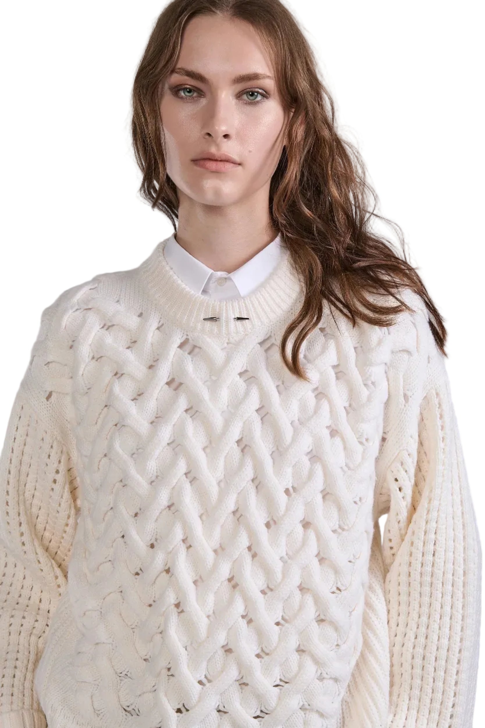 Woman wearing a white cable knit sweater over a white shirt against a plain background.
