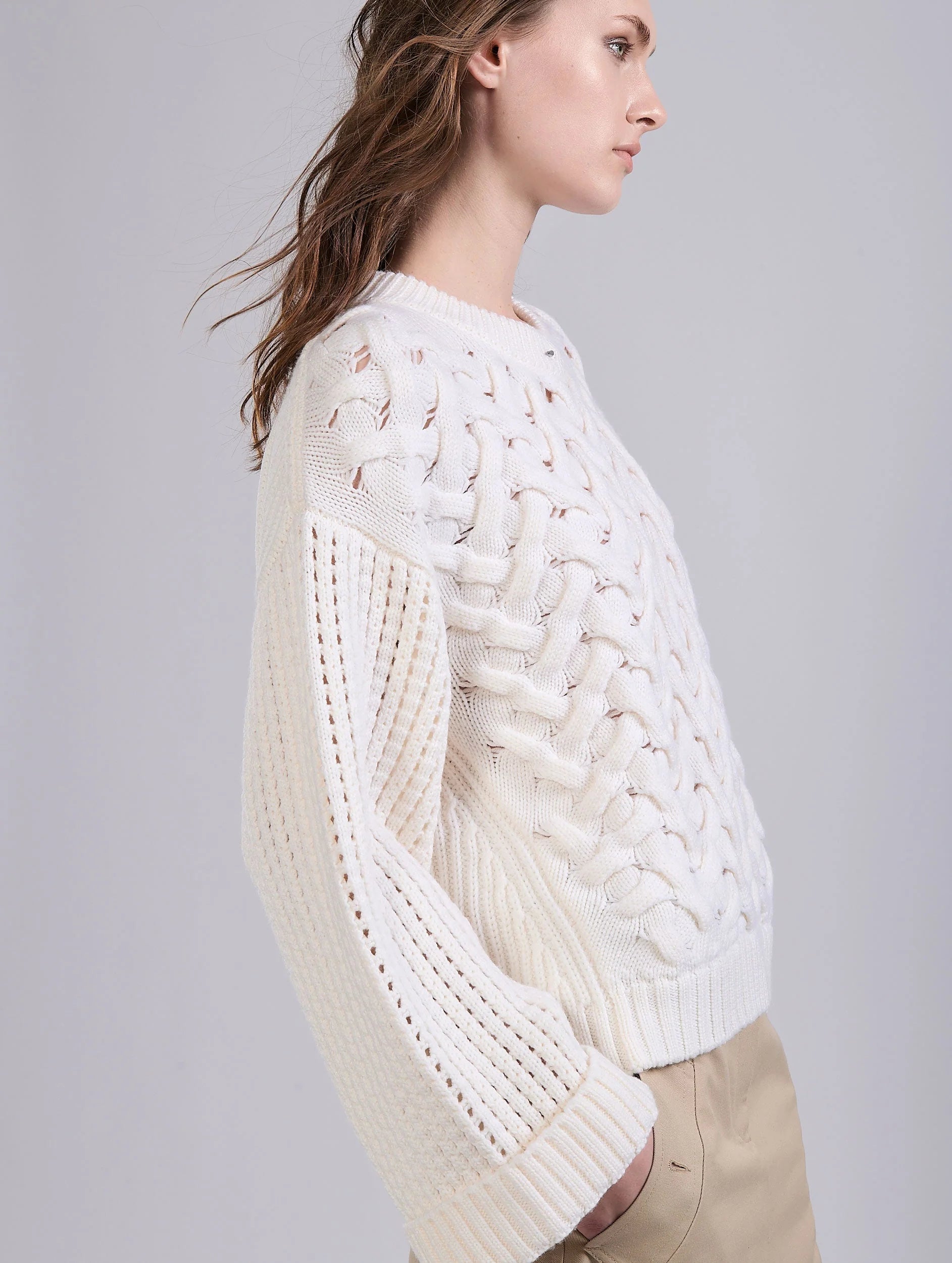 Woman wearing a white cable knit sweater on a light gray background.