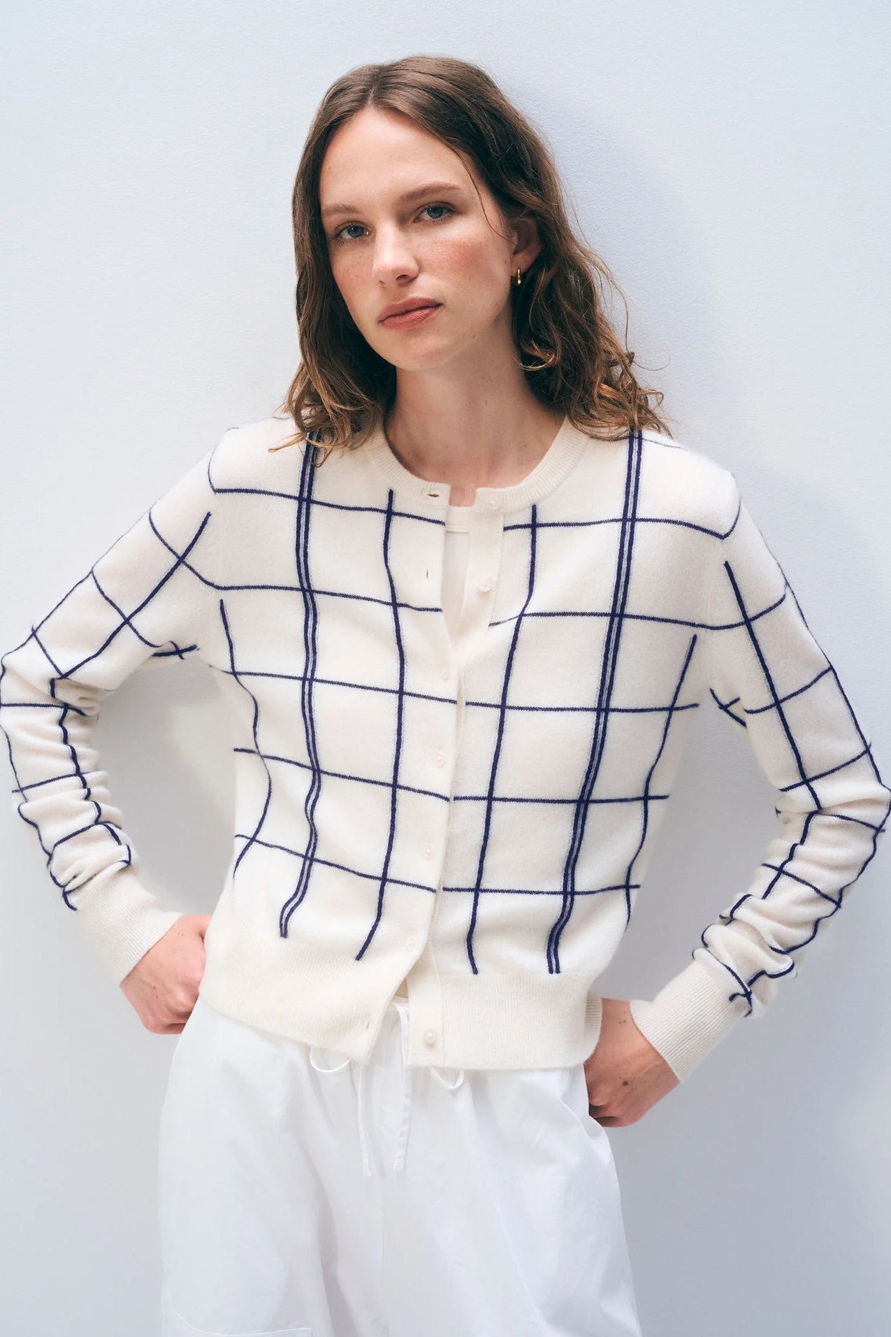 Woman wearing a white cardigan with blue windowpane pattern against a plain background.