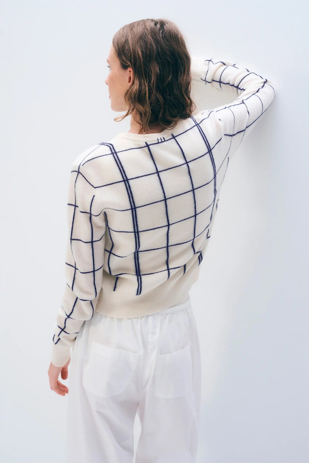 The back of a woman wearing a white sweater with blue checkered pattern against a light background.