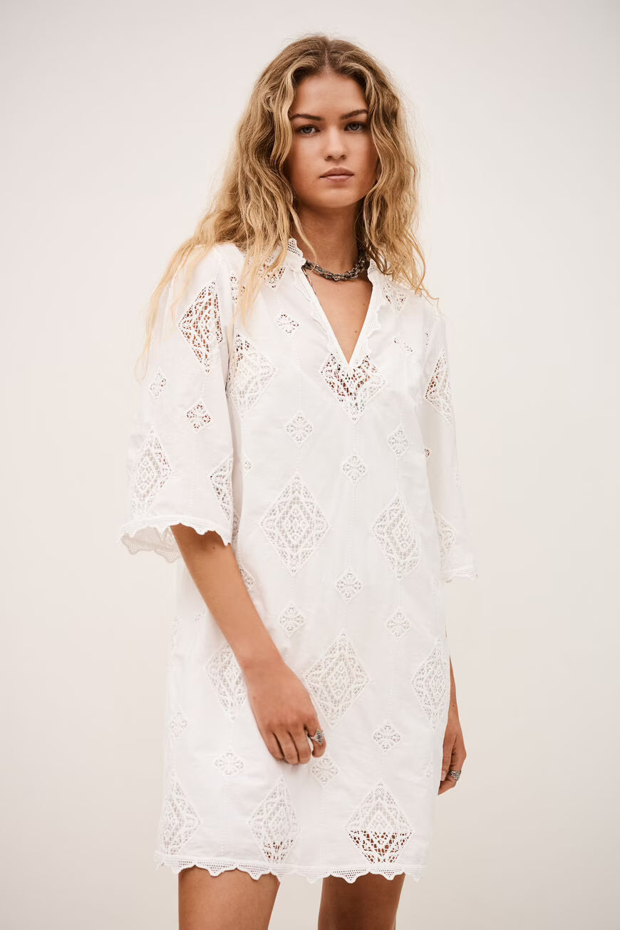 Woman wearing a white lace dress against a plain background.