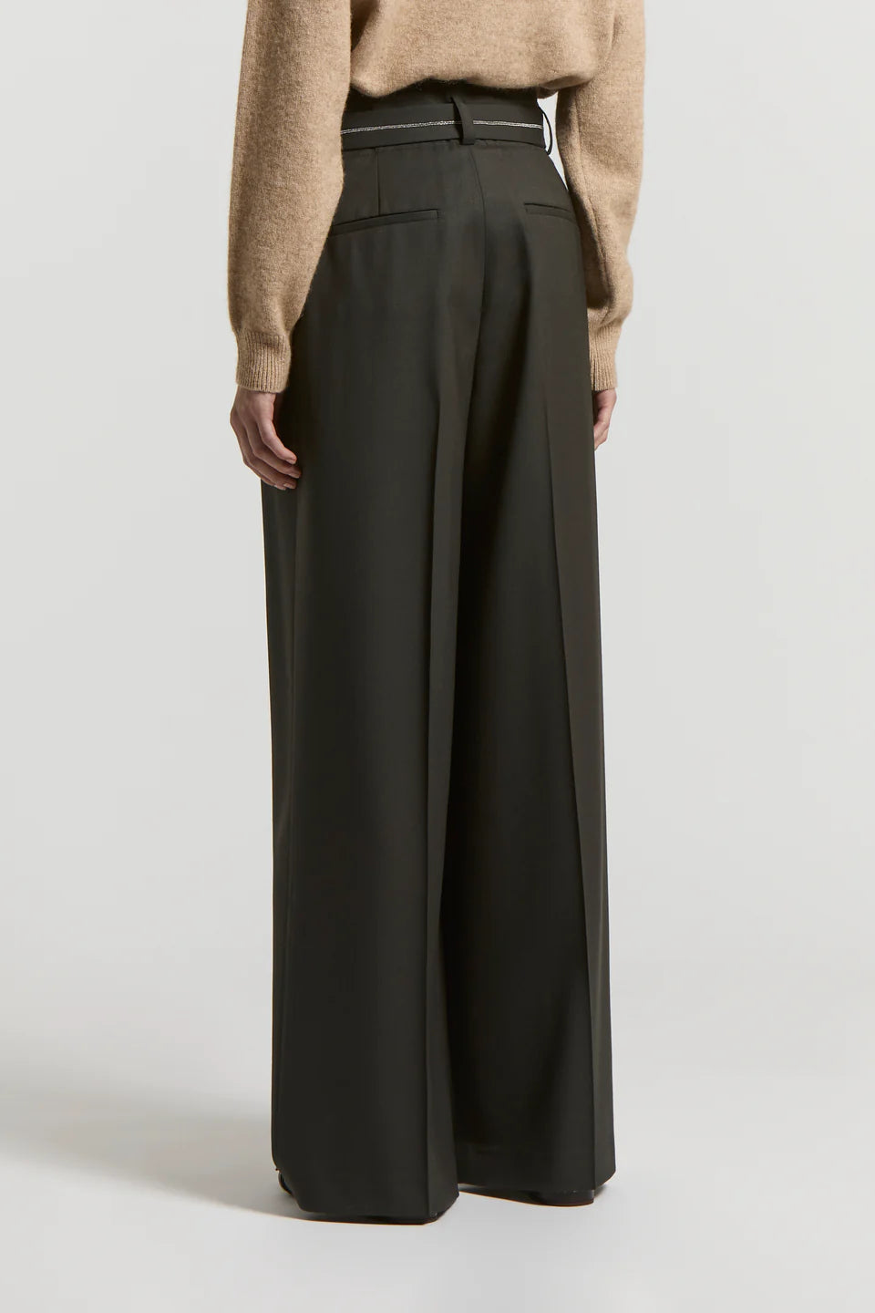 Back of a woman wearing black wide-leg pants with a sparkle belt and a beige sweater on a light background.